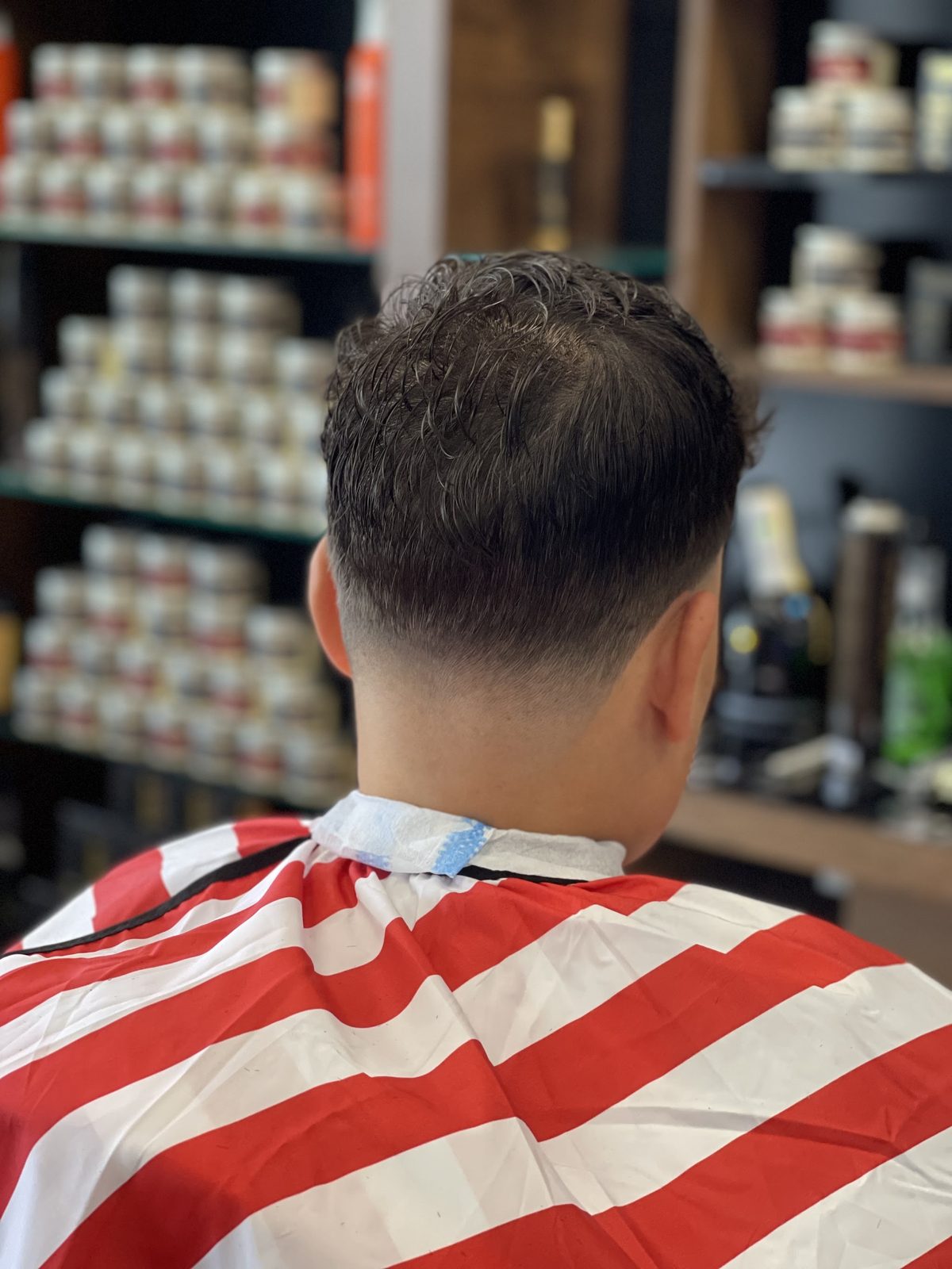 Kapsel van achteren, met de kast vol haarproducten van de zaak op de achtergrond